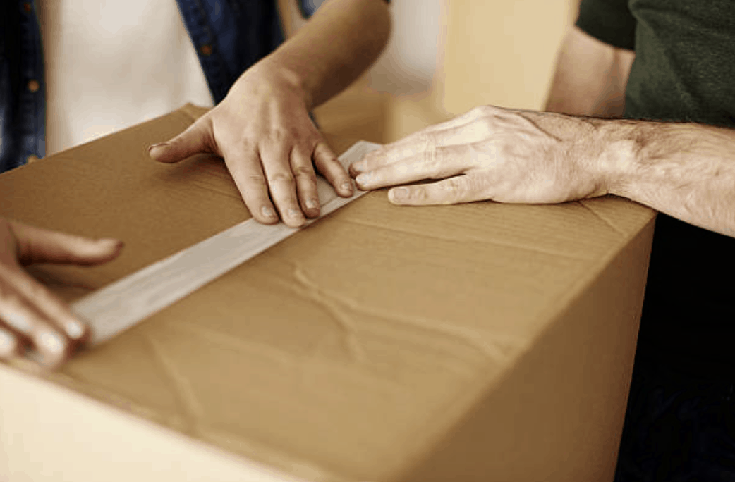 Two people taping a moving box shut