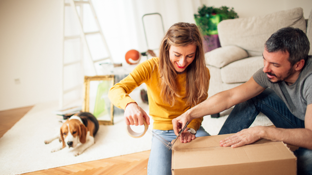 Couple taping up a moving box with a dog in the background