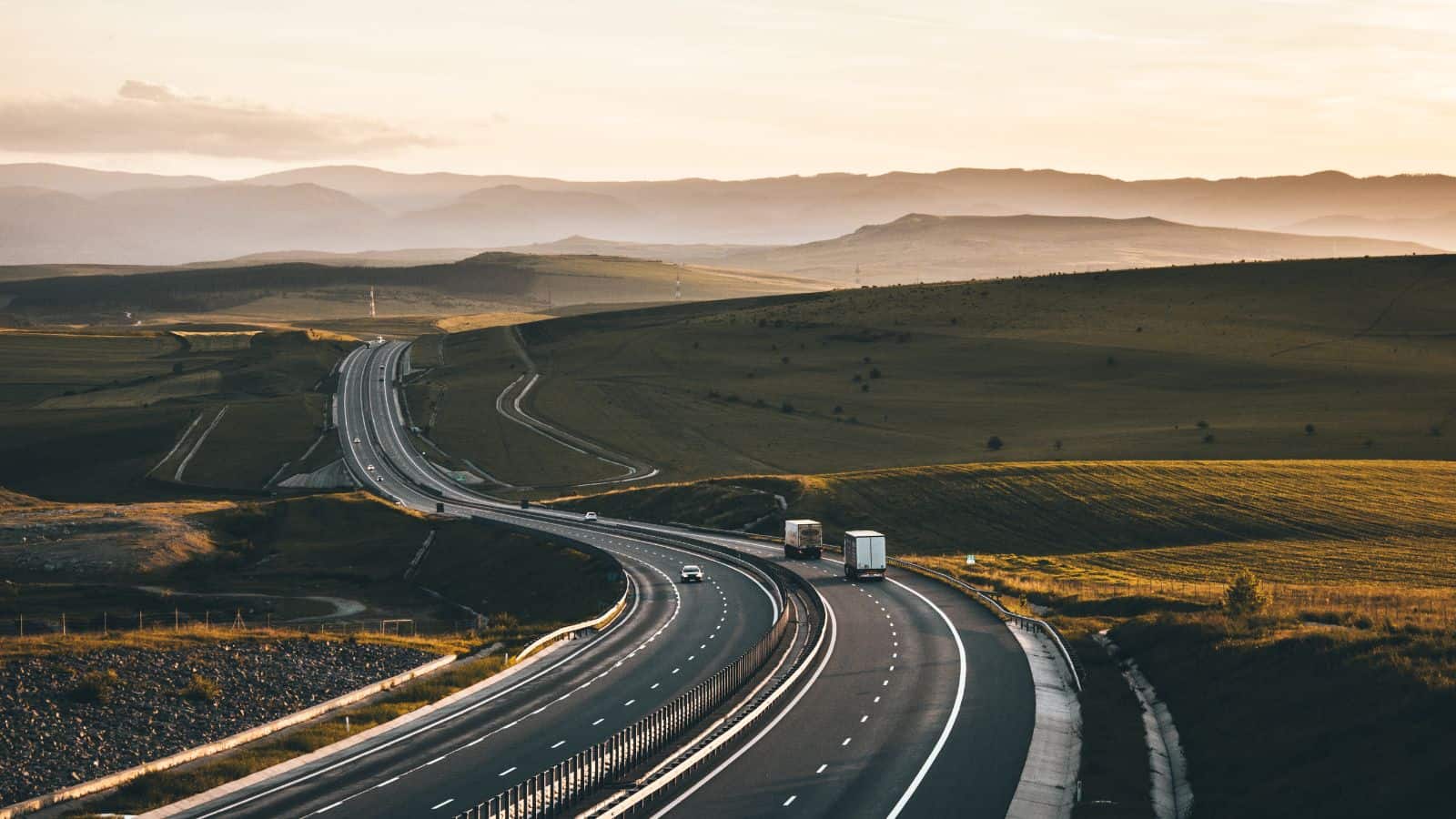 Trucks and cars driving on a highway through a hilly area of the country